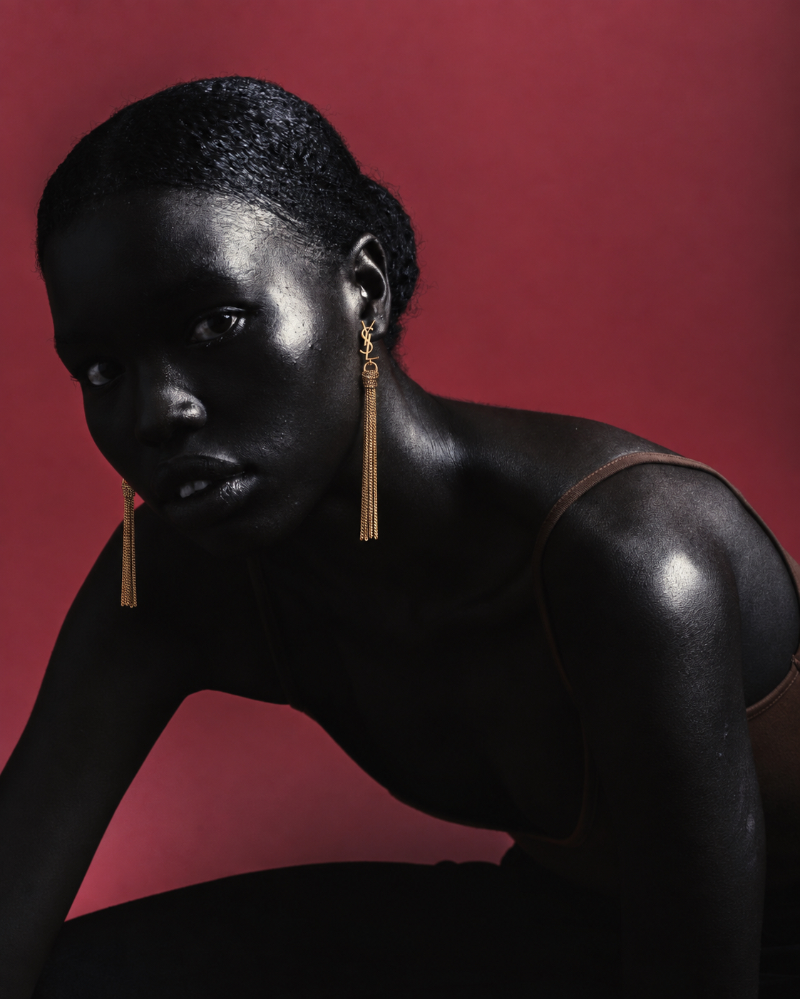 Model wearing long gold tassel earrings against a red background