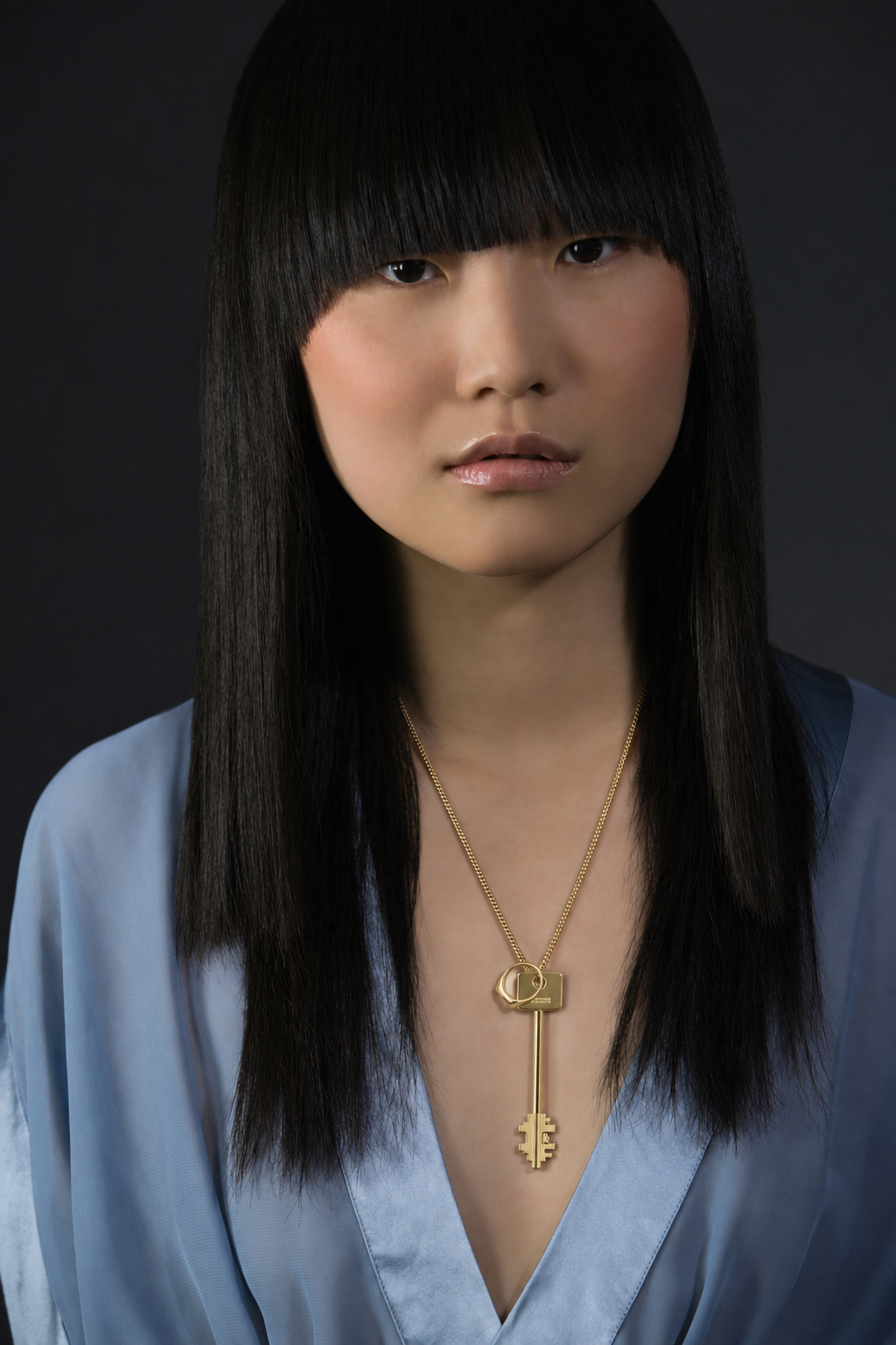 Model wearing a gold key pendant with a blue satin top
